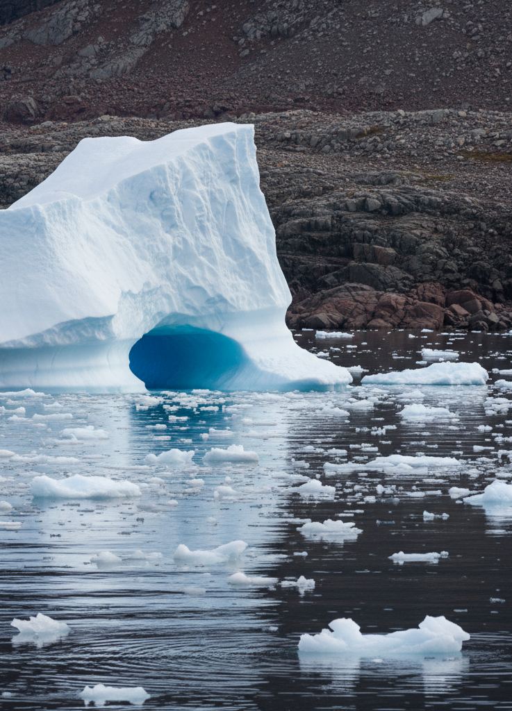 A grounded iceberg undercut at the waterline with small ice pieces floating around its base